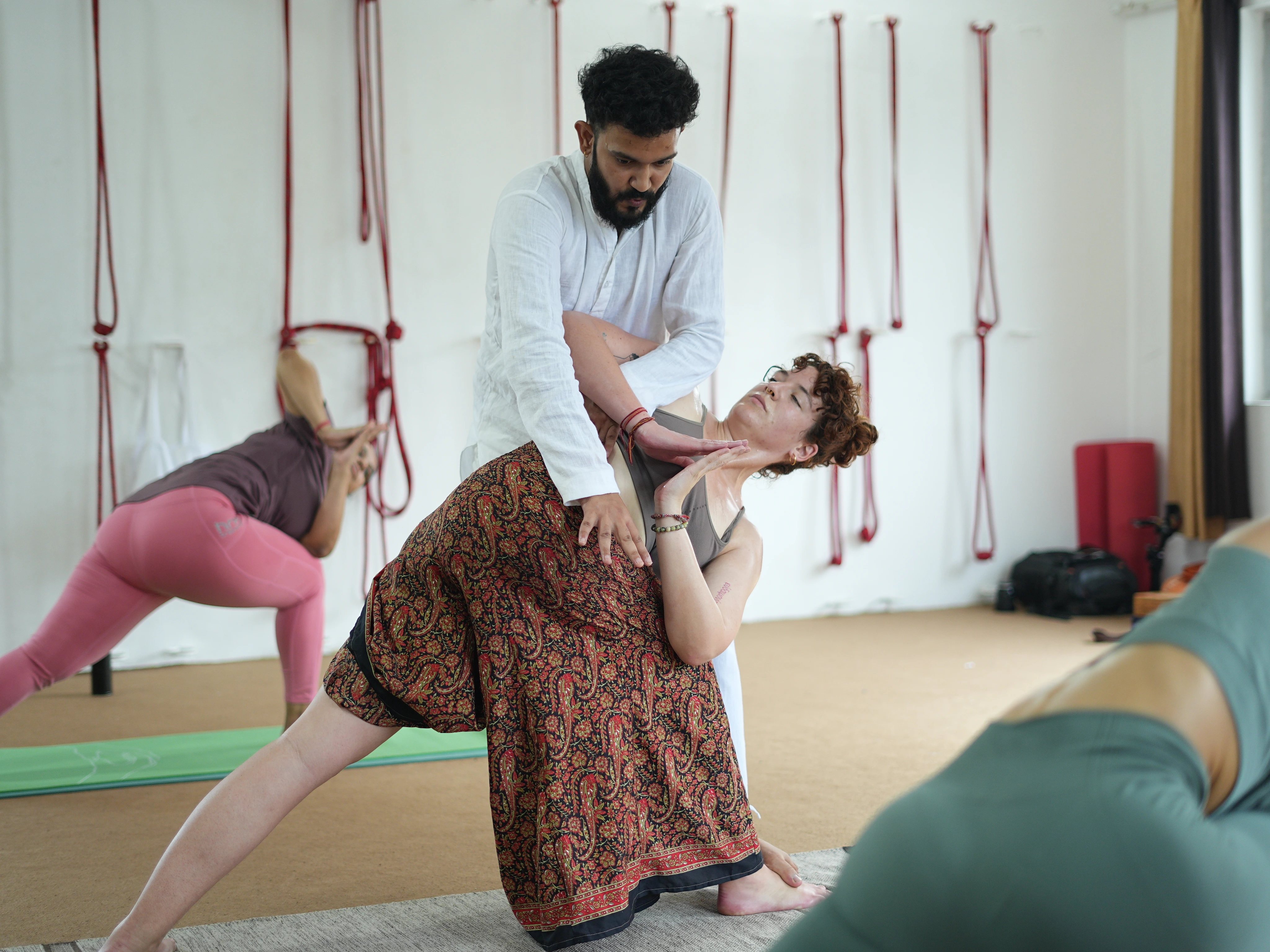 Yoga class with instructor guiding student in downward dog pose on yoga mats indoors
